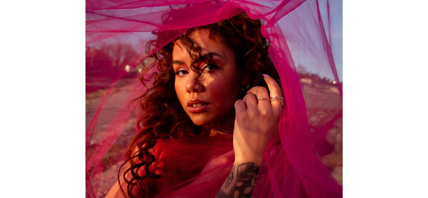 Woman with lustrous curly hair draped in pink veil at sunset